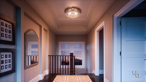 A hallway features framed photos, a large mirror, a patterned rug, and the Urban Ambiance UQL2081 Traditional Flush Mount Ceiling Light from the Manhattan Collection, showcasing a polished chrome finish. Sunlight streams through windows at the far end above a staircase with wooden railing.