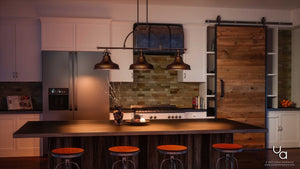 A modern kitchen with a dark island, three stools, and stainless appliances features the Urban Ambiance UQL2285 Industrial Chandelier (23.5″H x 52.5″W, Parisian Bronze Finish) from the Sonoma Collection as striking hanging lights with industrial-inspired detailing, as well as a sliding wooden barn door.
