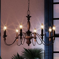 A unique Americana chandelier featuring a rustic bronze finish and six candles hanging in front of a window.