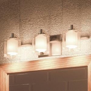 Three Urban Ambiance UQL2402 Modern Bathroom Vanity Lights from the Napa Collection, featuring frosted glass shades and a polished chrome finish (measuring 6″ high by 21″ wide), are installed above a mirror on a textured wall.