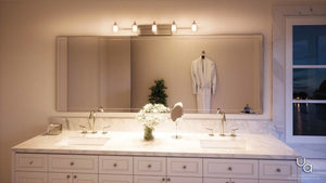 Certainly! Here’s the rewritten sentence integrating the provided product information: A double-sink bathroom vanity with a marble countertop is complemented by a large mirror, a flower vase, and elegant Urban Ambiance UQL2407 Modern Bathroom Vanity Light from the Napa Collection, featuring dual-layered glass and a polished chrome finish for contemporary style. A hanging robe and a window revealing an outdoor view complete the serene atmosphere.