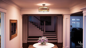 A bright entryway features a round table topped with a flower arrangement, a staircase in the background, framed wall art, and natural light streaming in from adjacent rooms. Anchoring the space overhead is the Urban Ambiance Genoa Collection UQL2435 Art Deco Semi-Flush Ceiling Light (12″H x 16″W) in a Copper Revival finish, casting a warm glow throughout the area.