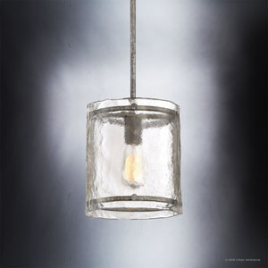 The Urban Ambiance UQL2871 Industrial Pendant from the Nantes Collection features a cylindrical glass shade with a textured, water-glass-like surface. Finished in Silver Etch and measuring 10 inches high by 9.25 inches wide, this light is suspended by a sleek metal rod and illuminated against a gradient background.