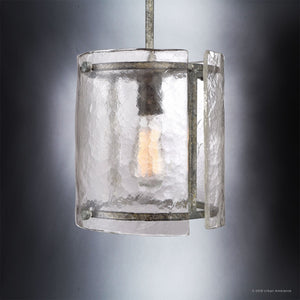 The UQL2871 Industrial Pendant from the Nantes Collection by Urban Ambiance features a central exposed bulb encased in textured, curved glass panels and a sturdy metal frame with a Silver Etch finish, measuring 10 inches high by 9.25 inches wide—an industrial-inspired pendant light displayed against a gradient gray background.