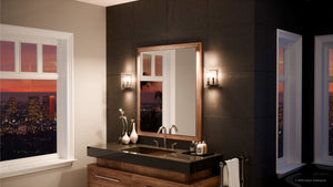 Modern bathroom with a wood-framed mirror, black countertop double sink, Urban Ambiance UQL2873 Industrial Wall Sconces in Silver Etch Finish from the Nantes Collection, and a large window showing a cityscape at sunset.