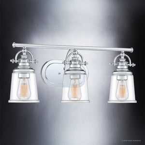 The Urban Ambiance UQL2881 Industrial Bathroom Vanity Light from the Salford Collection features three exposed filament bulbs set within clear glass shades, a polished chrome finish, and is mounted on a reflective wall plate. Measuring 9.5 inches high by 23 inches wide, it adds modern elegance to any bathroom setting.
