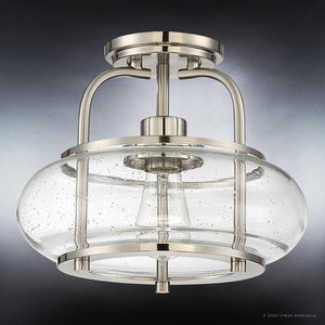 Introducing the UQL3280 Utilitarian Ceiling Light from Urban Ambiance’s Clearwater Collection, featuring a brushed nickel finish and a clear seeded glass shade with captivating air bubbles. Measuring 10″ high by 12″ wide and photographed against a gradient dark background, this elegant flush mount blends contemporary style with striking visual appeal to enhance any space.