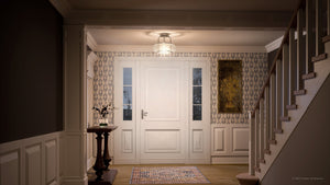 A well-lit entryway with a white front door, patterned wallpaper, wooden stairs, a small table with a vase, and a framed painting on the wall is beautifully illuminated by the Urban Ambiance UQL3280 Utilitarian Ceiling Light from the Clearwater Collection. Measuring 10 inches high by 12 inches wide and featuring a brushed nickel finish, this modern fixture adds contemporary elegance to the space.