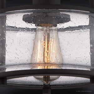 Close-up of the UQL3281 Utilitarian Ceiling Light by Urban Ambiance, featuring a vintage-inspired Edison bulb in an oversized clear seedy glass shade with a dark bronze frame. Part of the elegant Clearwater Collection, its textured glass imitates water droplets. Dimensions: 10