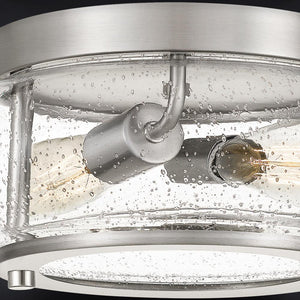 Close-up of the Urban Ambiance UQL3290 Utilitarian Ceiling Light from the Clearwater Collection, featuring a brushed nickel finish, ceiling-mounted design with two exposed bulbs, and a clear seeded glass cover with small air bubbles. Measures 5.75″H x 12″W.