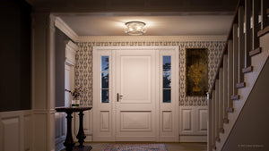 A hallway featuring a white front door, patterned wallpaper, a round table adorned with a vase, a framed painting, a staircase, and the Urban Ambiance UQL3290 Utilitarian Ceiling Light from the Clearwater Collection in brushed nickel finish (5.75″H x 12″W) with seeded glass.
