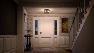 A dimly lit foyer includes a white door, patterned wallpaper, and a small table with a plant. To the right is a staircase adorned with Urban Ambiance's UQL3291 Utilitarian Ceiling Light from the Clearwater Collection in Dark Bronze, casting an inviting glow throughout the space.