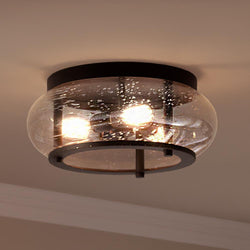 The UQL3301 Utilitarian Ceiling Light by Urban Ambiance features vintage-inspired bulbs in a circular transparent glass shade, mounted on a dark bronze base. Part of the Clearwater Collection, it measures 7" high by 16" wide.