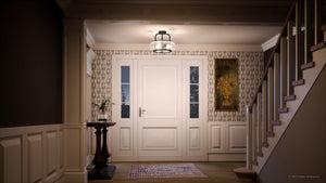 An elegant foyer features a central white door, two side windows, and floral wallpaper. A small table holds a vase on the left. Stairs ascend on the right, illuminated by the Urban Ambiance UQL3311 Utilitarian Ceiling Light with clear seedy glass shades from the Clearwater Collection.