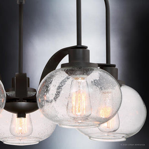 Close-up of the Urban Ambiance UQL3361 Utilitarian Chandelier, part of the Clearwater Collection, featuring three seedy glass shades and vintage bulbs in a dark bronze finish, casting a warm glow through the speckled texture.