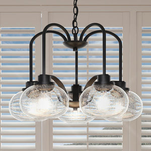 A unique chandelier, 19"H x 26.1"W, black bronze finish, from the Clearwater Collection hanging over a window with blinds.