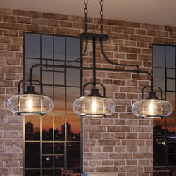 Three beautiful UQL3381 Utilitarian Chandeliers, 21.55"H x 38"W, with a Black Bronze Finish from the Clearwater Collection hanging over a brick wall in a kitchen