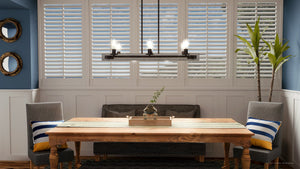 A dining room with blue walls and shutters adorned with the unique UQL3070 Utilitarian Chandelier by Urban Ambiance.