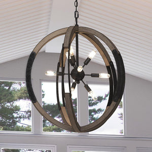 The Urban Ambiance UQL3110 XL Urban Loft Chandelier from the Abilene Collection, featuring weathered black finish and wooden rings, hangs in a room with large windows and a white paneled ceiling.