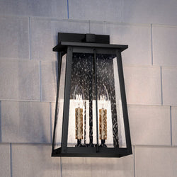 A luxurious UEX1022 Craftsman Outdoor Wall Sconce in a gorgeous Matte Black & Native Brass Finish from the Athens Collection by Urban Ambiance, beautifully illuminates a white wall.
