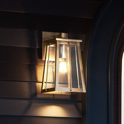 A unique UEX1025 Craftsman Outdoor Wall Sconce with an Antique Brass Finish, from the Athens Collection by Urban Ambiance, beautifies the side of a house.