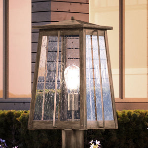 An Urban Ambiance UEX1029 Craftsman Outdoor Post Light 17''H x 9''W, Antique Brass Finish, Athens Collection gorgeous lighting fixture with a lamp on a wooden post.