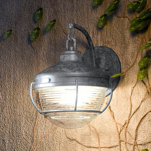 An Urban Ambiance UEX1056 Nautical Outdoor Wall Sconce, a unique lighting fixture,  is hanging on a wall next to a plant.