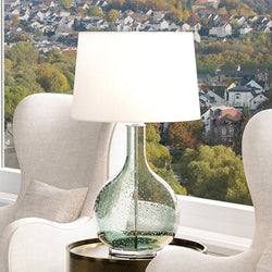 A beautiful lighting fixture, the UEX7040 Contemporary Table Lamp with a clear green finish from the Winslow Collection by Urban Ambiance, sits on a table in front of a window.