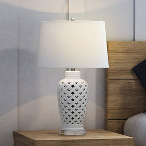 A luxury lamp, the UEX7180 Cottage Table Lamp from the Gruene Collection by Urban Ambiance, illuminates a wooden nightstand with its clear and white finish.