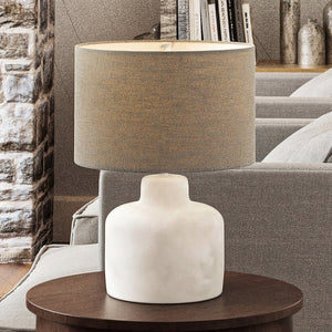 A gorgeous organic table lamp with a unique polished concrete finish from the Stuart Collection, featuring a tan shade, in a living room.