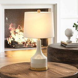 A unique lighting fixture - the Urban Ambiance UEX7450 Transitional Table Lamp from the Damascus Collection boasts a Cream and Aged Brass finish, placed on a wooden table in front of a fireplace.