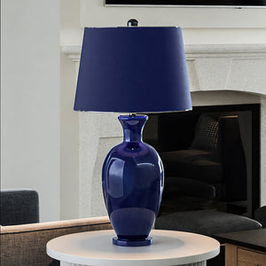 A beautiful UEX7480 Glam Table Lamp with a Navy Blue and Black Nickel Finish from the Genevieve Collection by Urban Ambiance on a table in a living room.