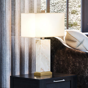 A luxurious glamourous table lamp from the Fairfield Collection by Urban Ambiance, featuring a unique white stone and gold leaf finish, placed on a table next to a window.