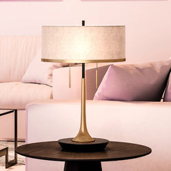 A gorgeous lighting fixture, the UEX7740 Glam Table Lamp in brass and black finish from the Aspen Collection by Urban Ambiance, enhances a living room with a pink couch.
