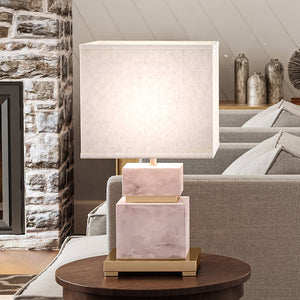 A beautiful and unique UEX7880 Glam Table Lamp from the Silverton Collection by Urban Ambiance, with a natural pink and bronze finish, placed on a table in front of a fireplace.