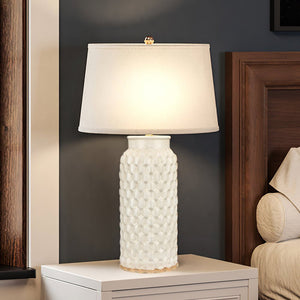 A unique and luxury UEX7910 Modern-Rustic Table Lamp from the Keystone Collection, with a White Glazed Finish, adds urban ambiance on a nightstand next to a bed.