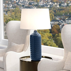 A unique coastal table lamp with a navy blue finish from the Apex Collection adds a gorgeous ambiance when placed on a table in front of a window.