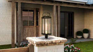 A unique outdoor lamp from the Orlando Collection, featuring an Olde Bronze finish and placed on a stone ledge in front of a house.