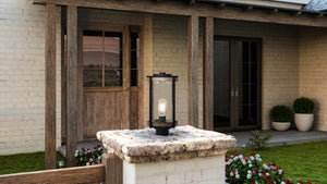 A beautiful Urban Ambiance UHP1353 Farmhouse Outdoor Post Light with a Midnight Black Finish, showcased on a stone wall in front of a house.