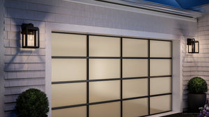 A modern garage door with frosted glass panels, flanked by two Urban Ambiance UHP1386 Marine-Grade Midnight Black outdoor wall sconces from the Macon Collection, and potted shrubs on either side.