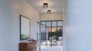 A hallway with beautiful glass doors and a gorgeous painting on the wall, illuminated by the UHP3923 Industrial Ceiling Light.