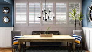 An Urban Ambiance dining room with unique blue walls and shutters, lit by a stylish lighting fixture.