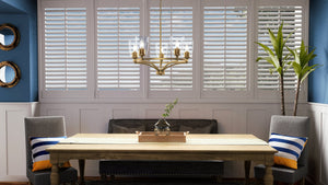 A beautiful dining room with blue walls and white shutters featuring the UHP4251 Traditional Chandelier 12.5''H x 25.25''W, Brushed Bronze Finish from Urban