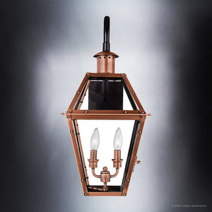 The Urban Ambiance UQL1382 Historic Outdoor Wall Light from the Paris Collection features a rustic copper finish, black handle, and clear glass panels. Measuring 22.5 inches high by 10.5 inches wide, this handcrafted lantern showcases two exposed light bulbs for vintage outdoor charm and timeless appeal. Photographed on a neutral gradient background, it can be used as an elegant wall sconce to elevate any space.
