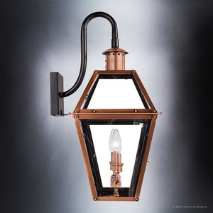 The Urban Ambiance UQL1382 Historic Outdoor Wall Light from the Paris Collection, featuring a handcrafted design with a rustic copper finish, a glass enclosure, and a single exposed bulb, serves as an elegant 22.5″H x 10.5″W wall sconce mounted on a black metal bracket against a gray background. This vintage-inspired outdoor lighting fixture adds timeless charm to any exterior space.