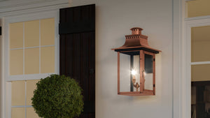The UQL1411 Vintage Outdoor Wall Light from Urban Ambiance’s Longview Collection showcases handcrafted outdoor lighting in a 23-inch tall, 12-inch wide lantern-style design with a rustic copper finish. Mounted on an exterior wall near a window, black shutter, and potted round shrub, this striking piece brings classic charm to your home’s outdoor space.