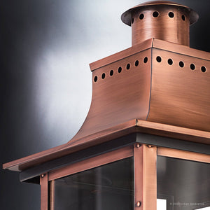 Close-up of the Urban Ambiance UQL1411 Vintage Outdoor Wall Light from the Longview Collection, showcasing its rustic copper-finished metal frame with a vented top and glass panels, displayed against a neutral background.