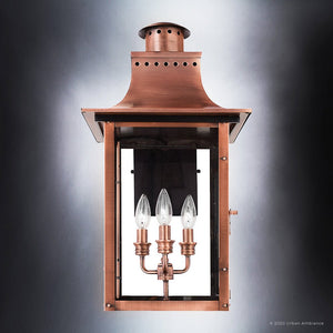 The Urban Ambiance UQL1411 Vintage Outdoor Wall Light from the Longview Collection features a handcrafted rectangular glass housing, vented top, and three candle-style light bulbs inside that capture the charm of a vintage lantern light. Measuring 23″H x 12″W and finished in rustic copper, this outdoor lighting piece is photographed against a gradient background, accentuating its timeless appeal.