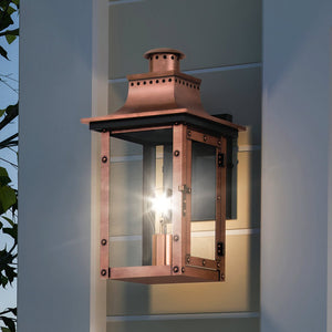 The UQL1413 Vintage Outdoor Wall Light from Urban Ambiance’s Longview Collection, featuring a rustic copper finish and clear glass design, mounts elegantly on your wall—its exposed bulb casting a beautiful glow against light gray siding at dusk and capturing the timeless charm of a classic gaslight lantern.