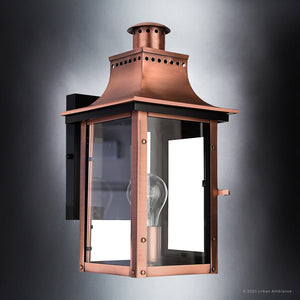 The UQL1413 Vintage Outdoor Wall Light from the Longview Collection by Urban Ambiance features a rustic copper finish and clear glass panels, mounted on a black rectangular base with an exposed bulb that evokes a classic gaslight lantern look. Handcrafted for quality, this 15.3″H x 7.75″W outdoor lighting piece brings timeless charm to any exterior space.